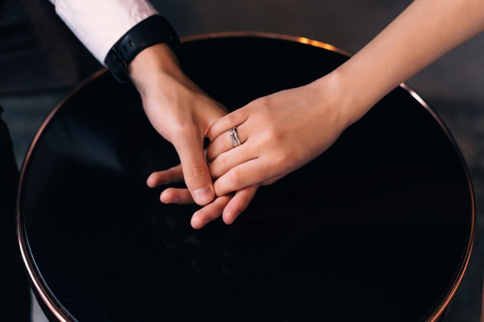 peelerie Beautiful and expensive wedding ring on a womans finger Couple holding hands over table Close up